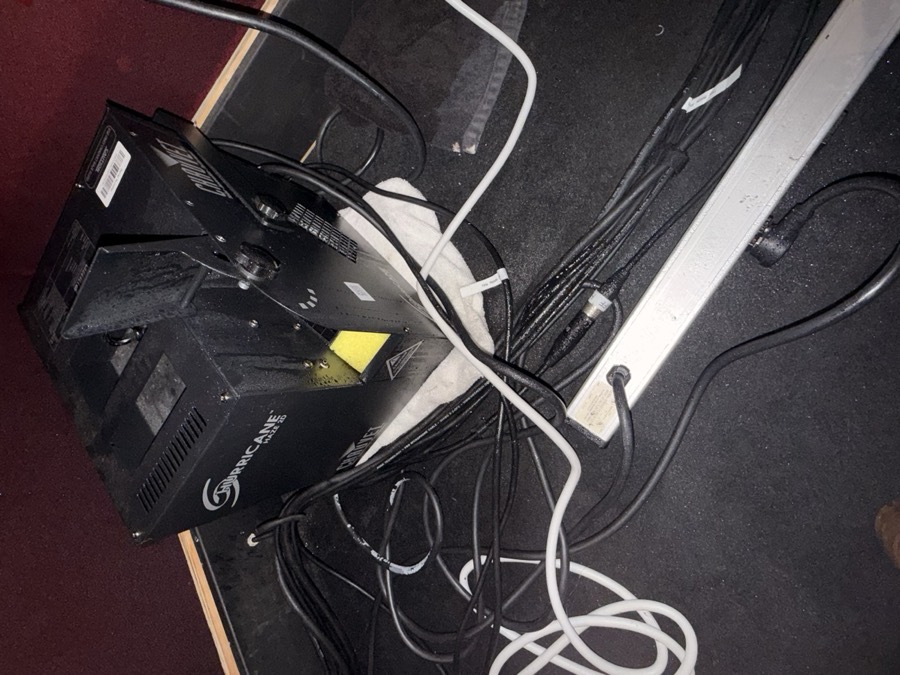 Fog machine on a towel beside a power strip and loose cables